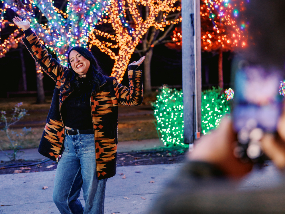 Woman joyously dancing at Tulalip Casino Resort's Amphitheatre in front of trees covered fully with brilliant and colorful Christmas lights.